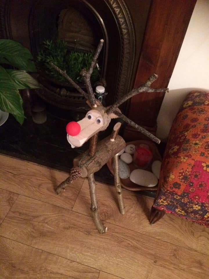 Handmade reindeer sculpture from twigs and wood, with a red nose, indoors.