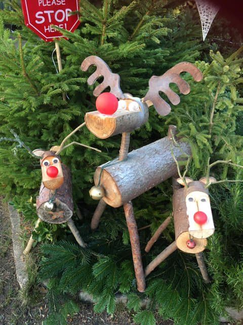 Three wooden reindeer with red noses and antlers stand in front of evergreen branches.