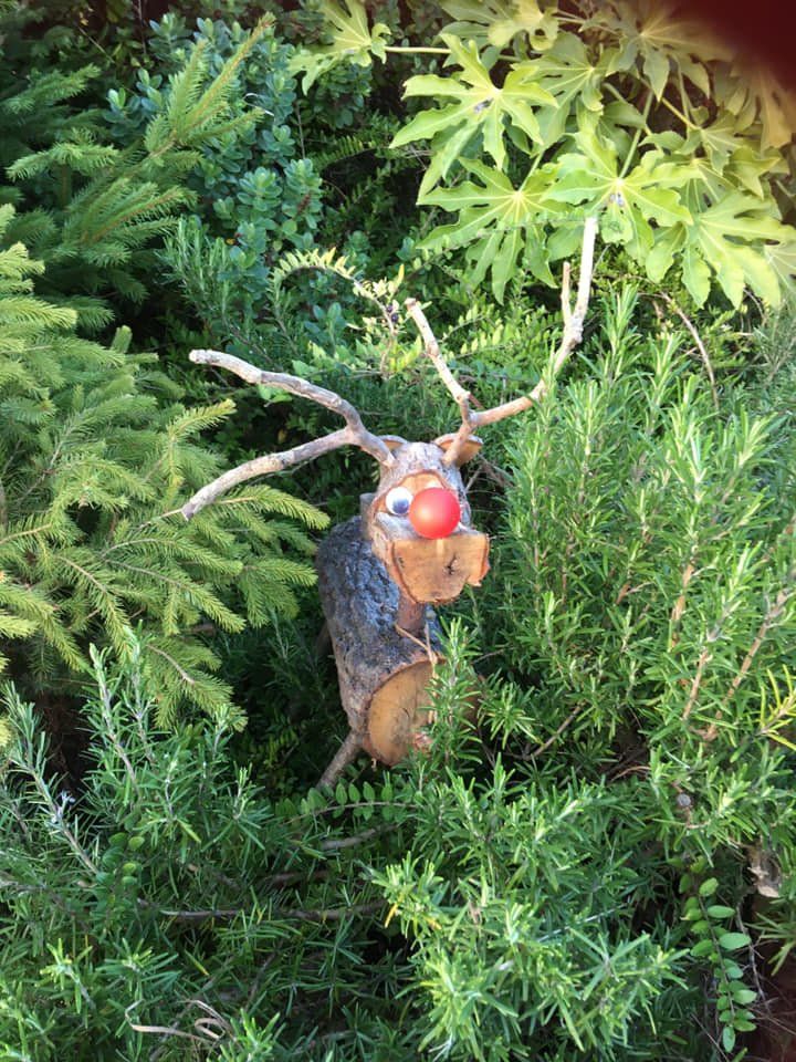 Wooden reindeer decoration with red nose, antlers, and greenery background.