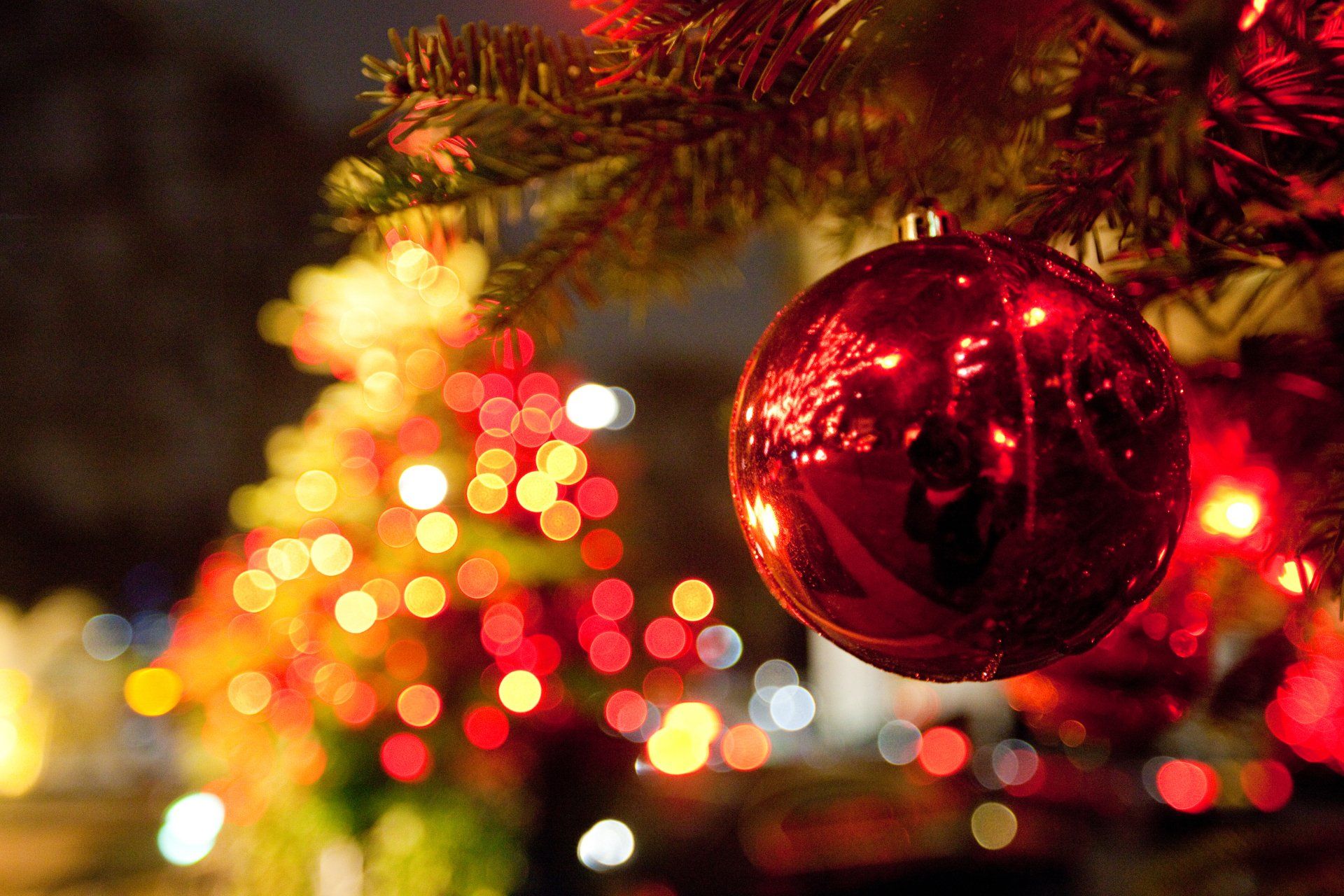 Red Christmas ornament hanging on a tree, surrounded by blurry colorful lights.
