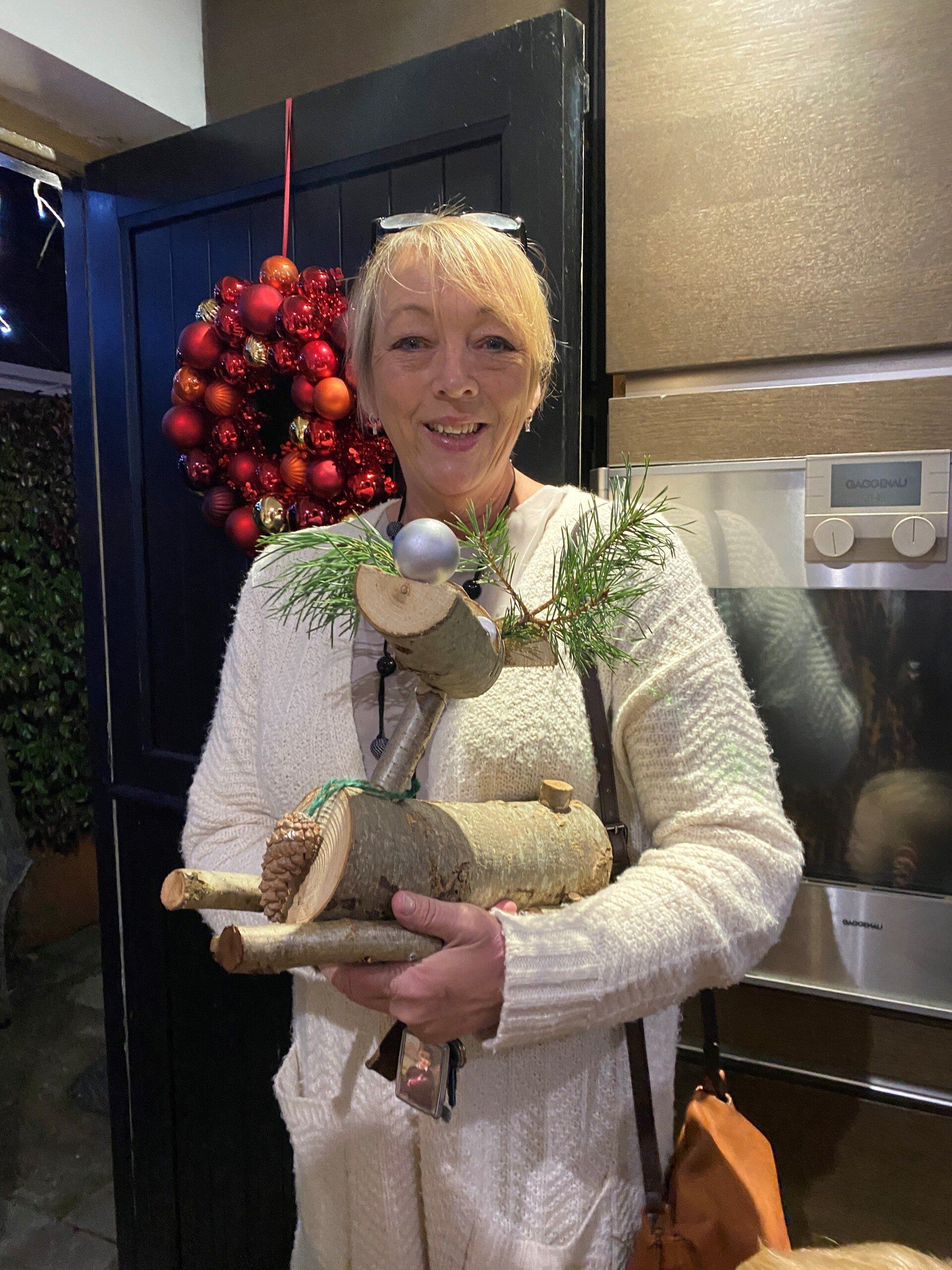 Woman holding a wooden reindeer decoration, standing by a door with a holiday wreath.