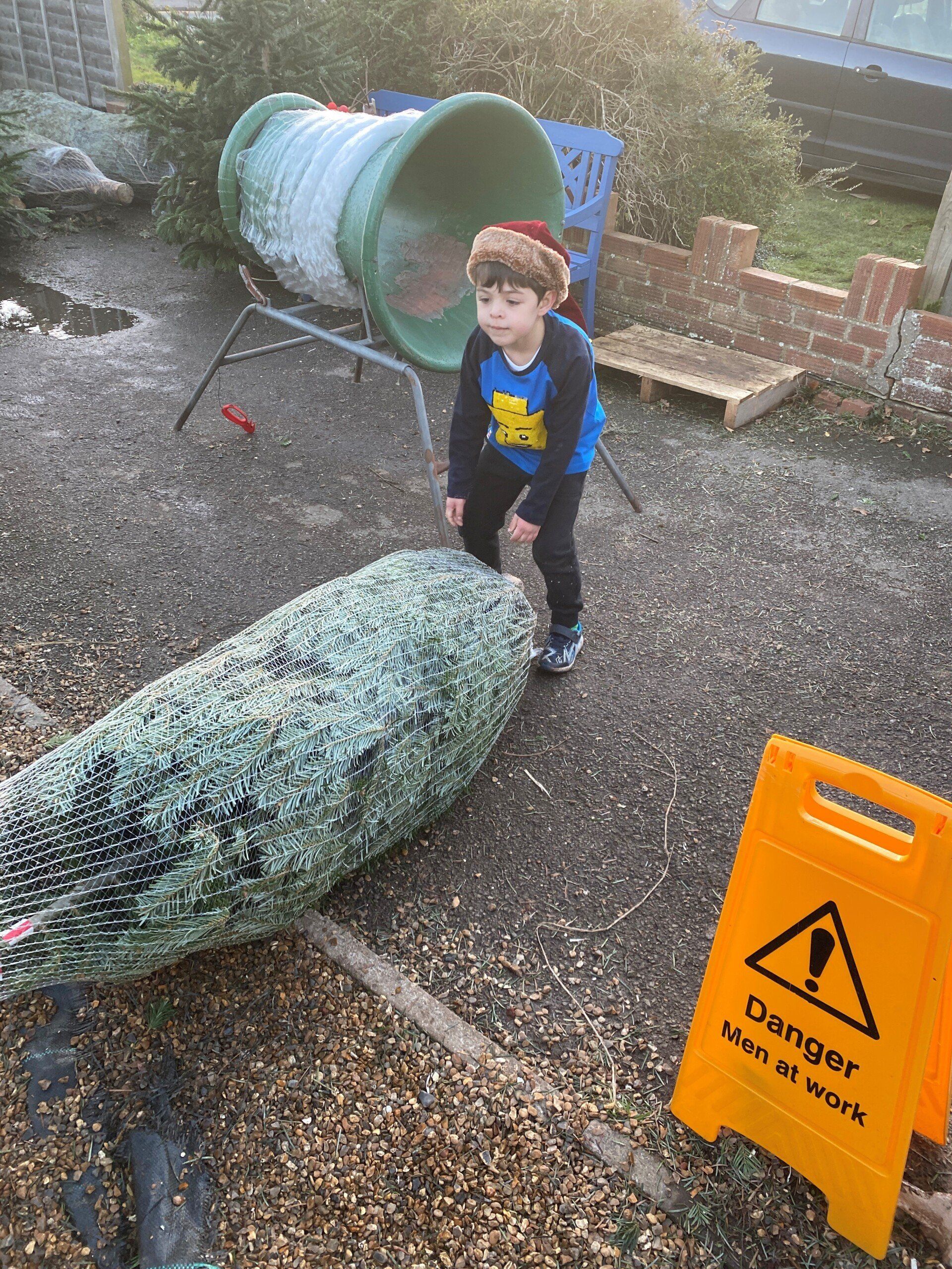 Child in Santa hat near large green lizard sculpture and a danger sign.