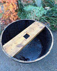 Wooden barrel with a wooden plank and a square hole in the center, outdoors.