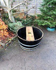 Black wooden barrel planter with wooden plank, outdoors.