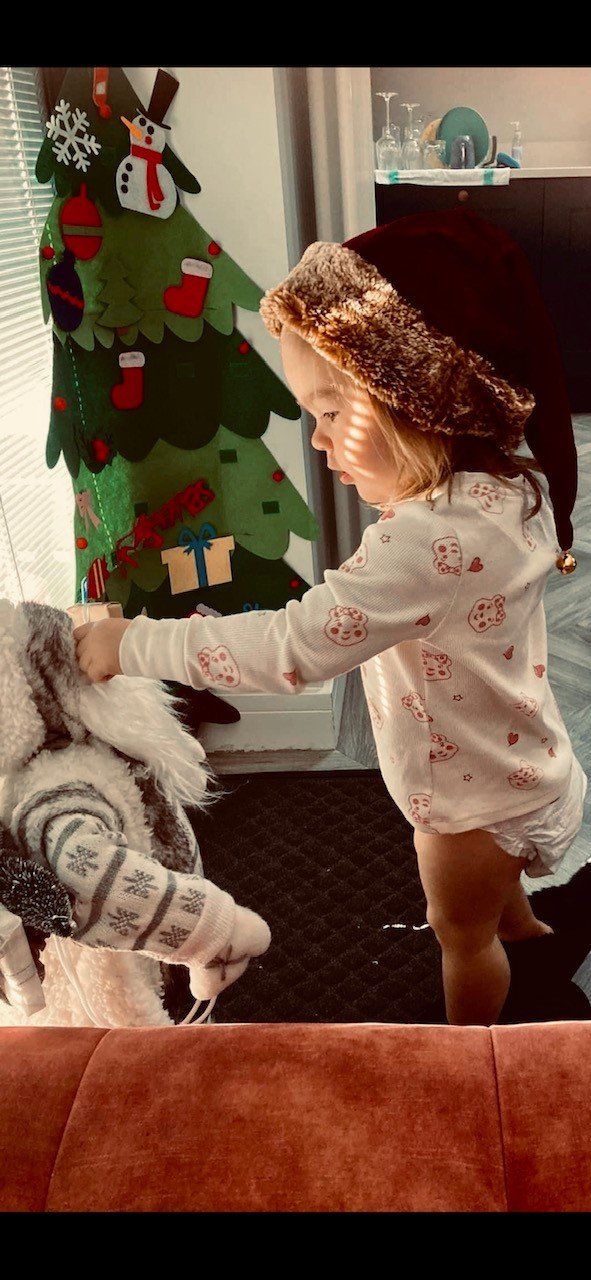 Child reaching for a blanket near a Christmas tree decoration.