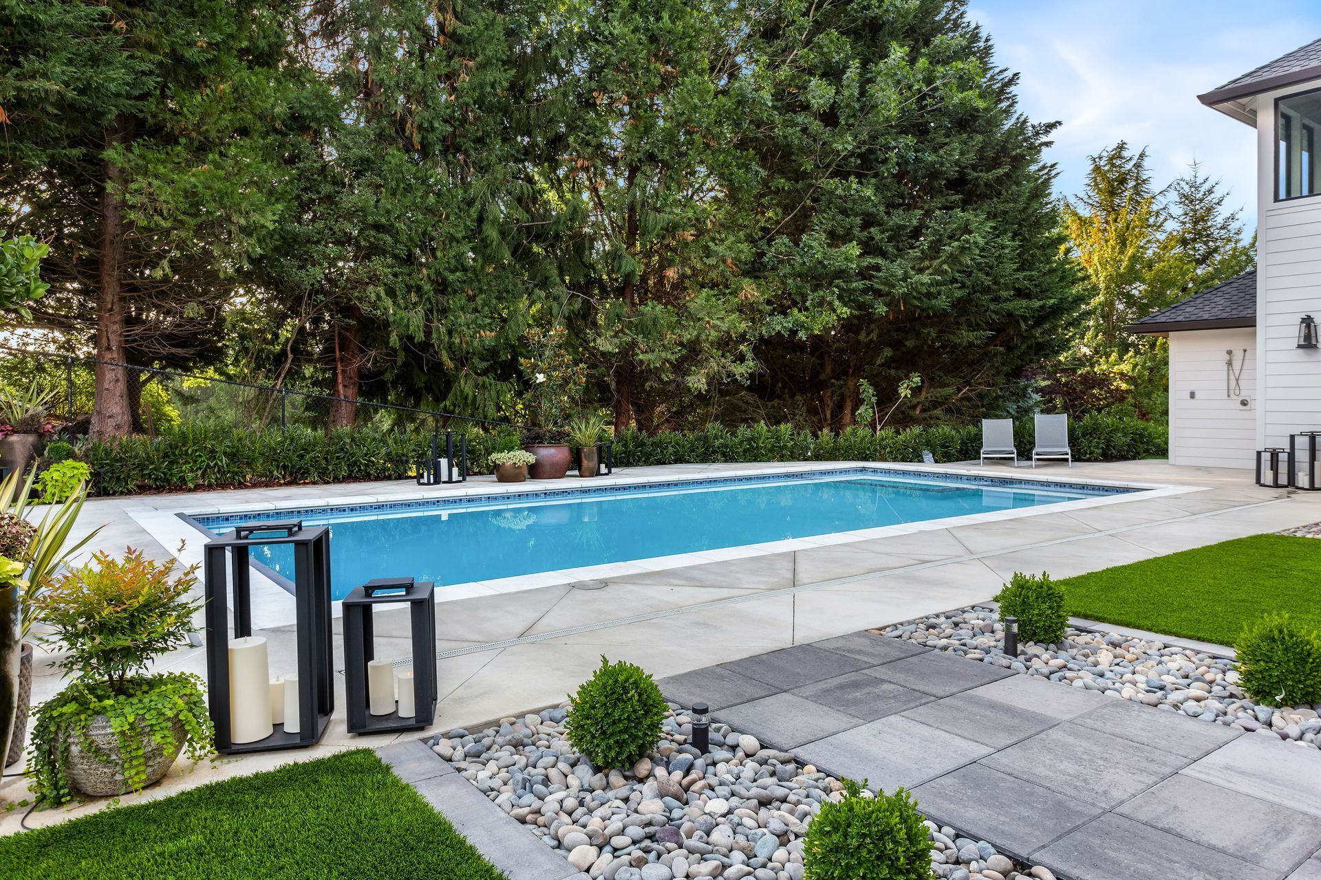 Modern backyard with a rectangular swimming pool, patio, landscaping, and lounge chairs.