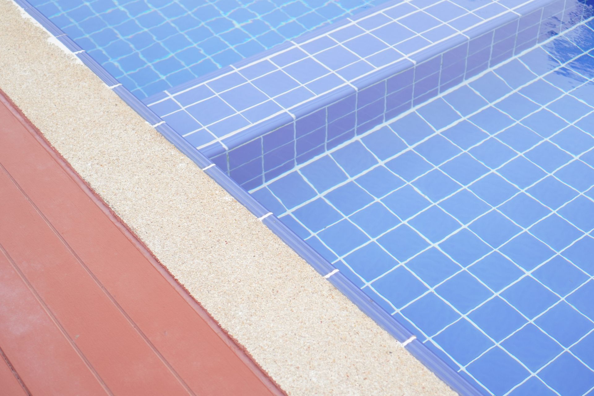 Pool edge with blue tiles, beige border, and red deck.