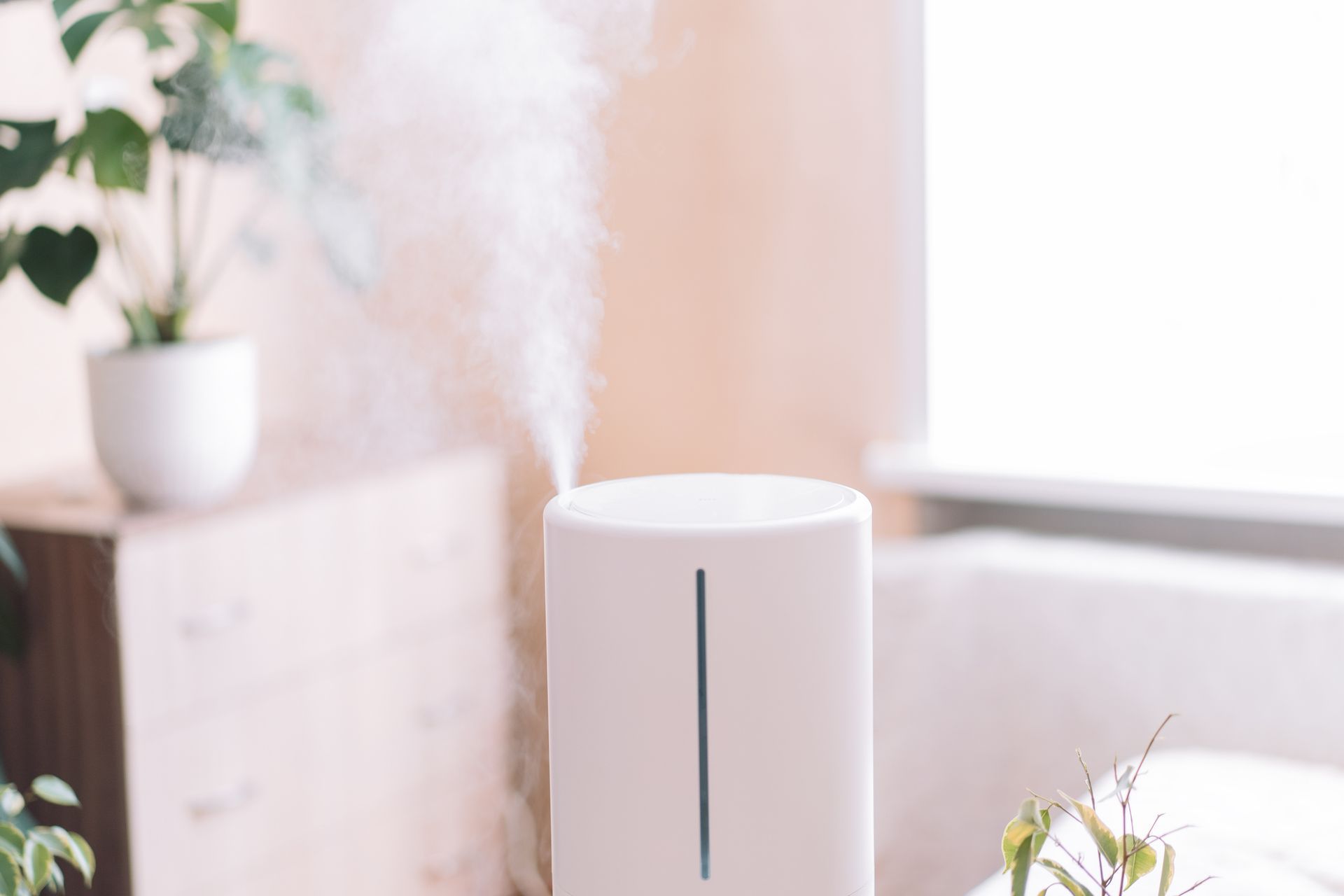 A white humidifier is sitting in a living room next to a window. A white humidifier is sitting in a living room next to a window.