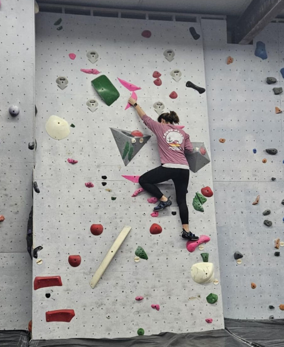 Person climbing a colorful indoor rock wall, reaching for a hold.
