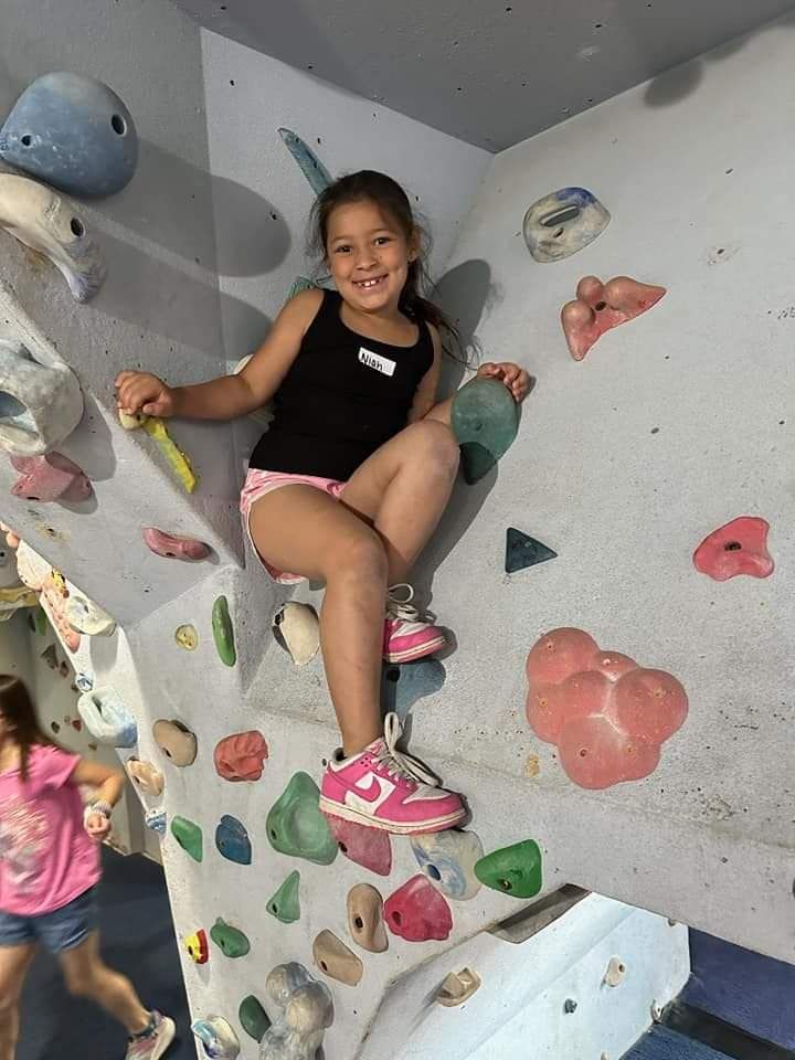 Girl smiling while climbing a colorful indoor rock wall.