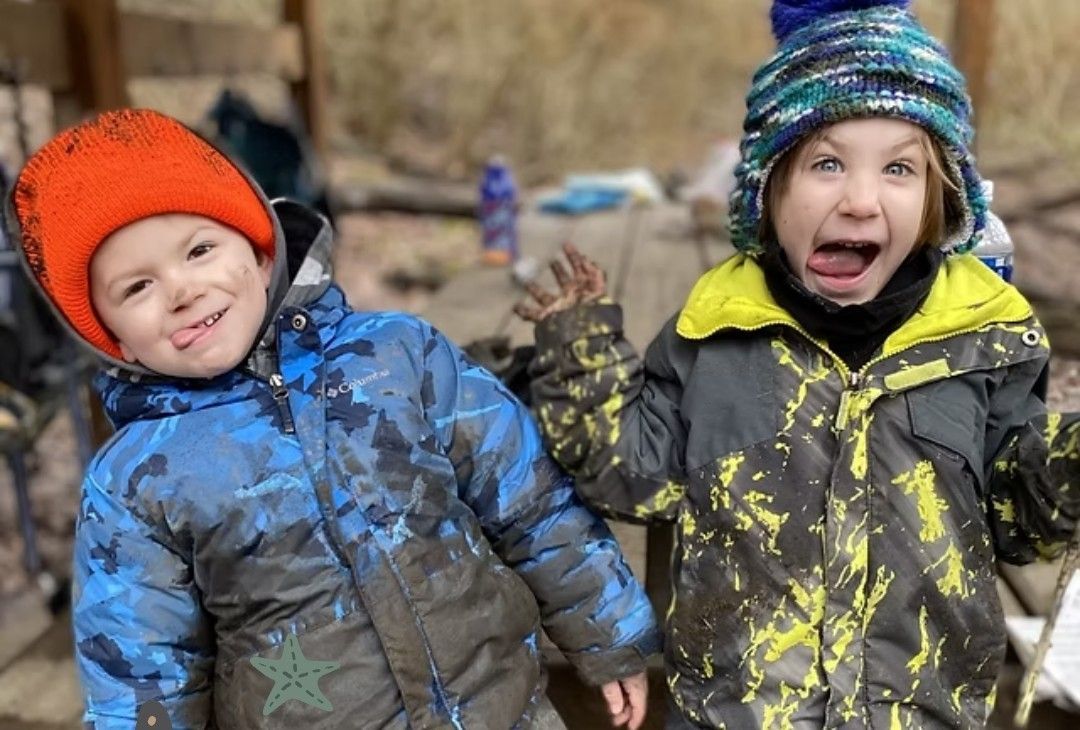 Two children covered in mud, one smiling with tongue out, the other with surprised expression, outside.