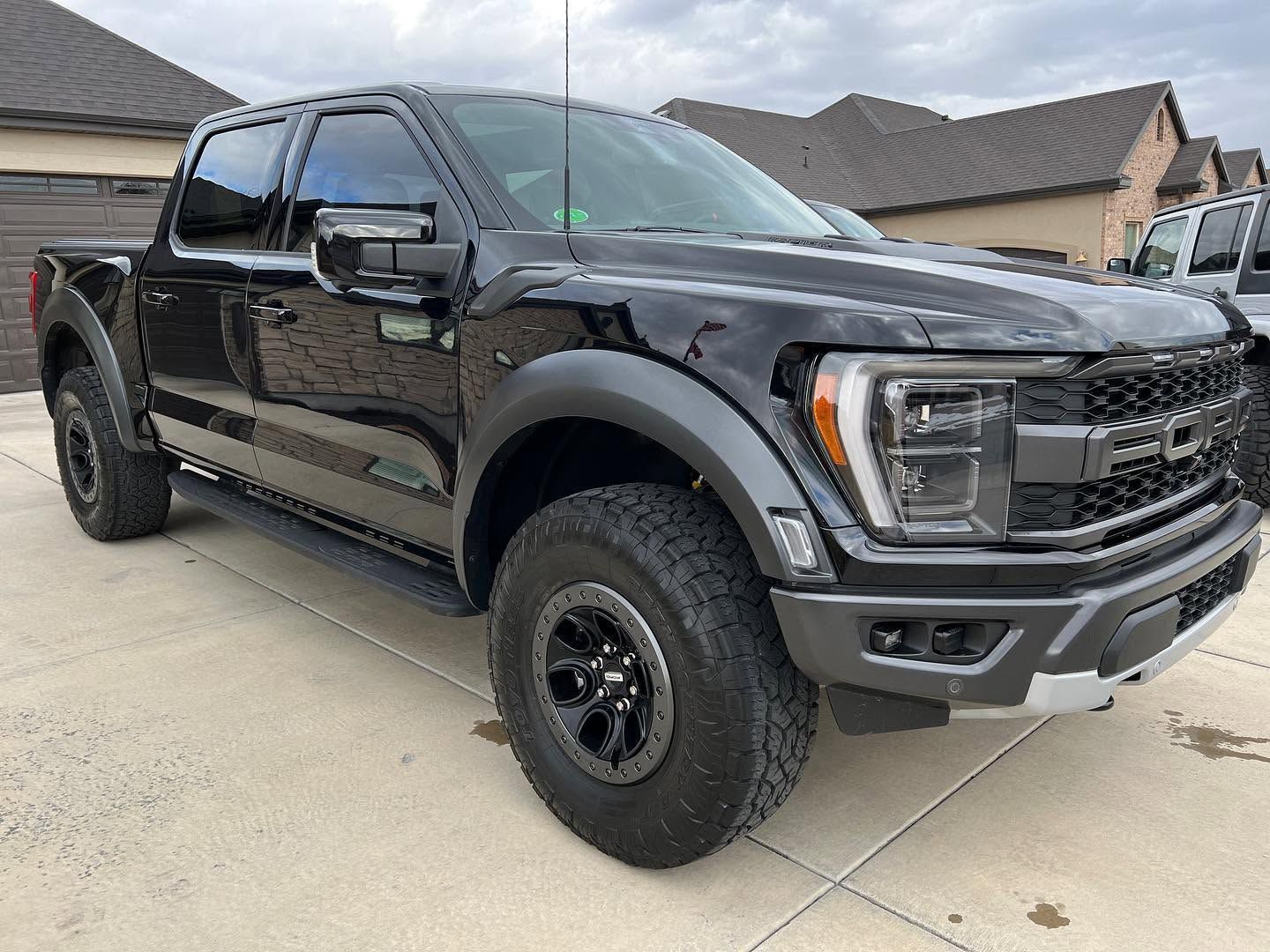 Black lifted pickup truck parked in a driveway, front three-quarter view