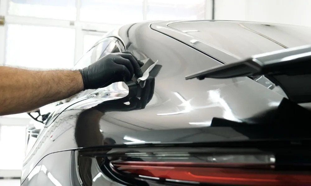 A man is polishing the hood of a car in a garage.