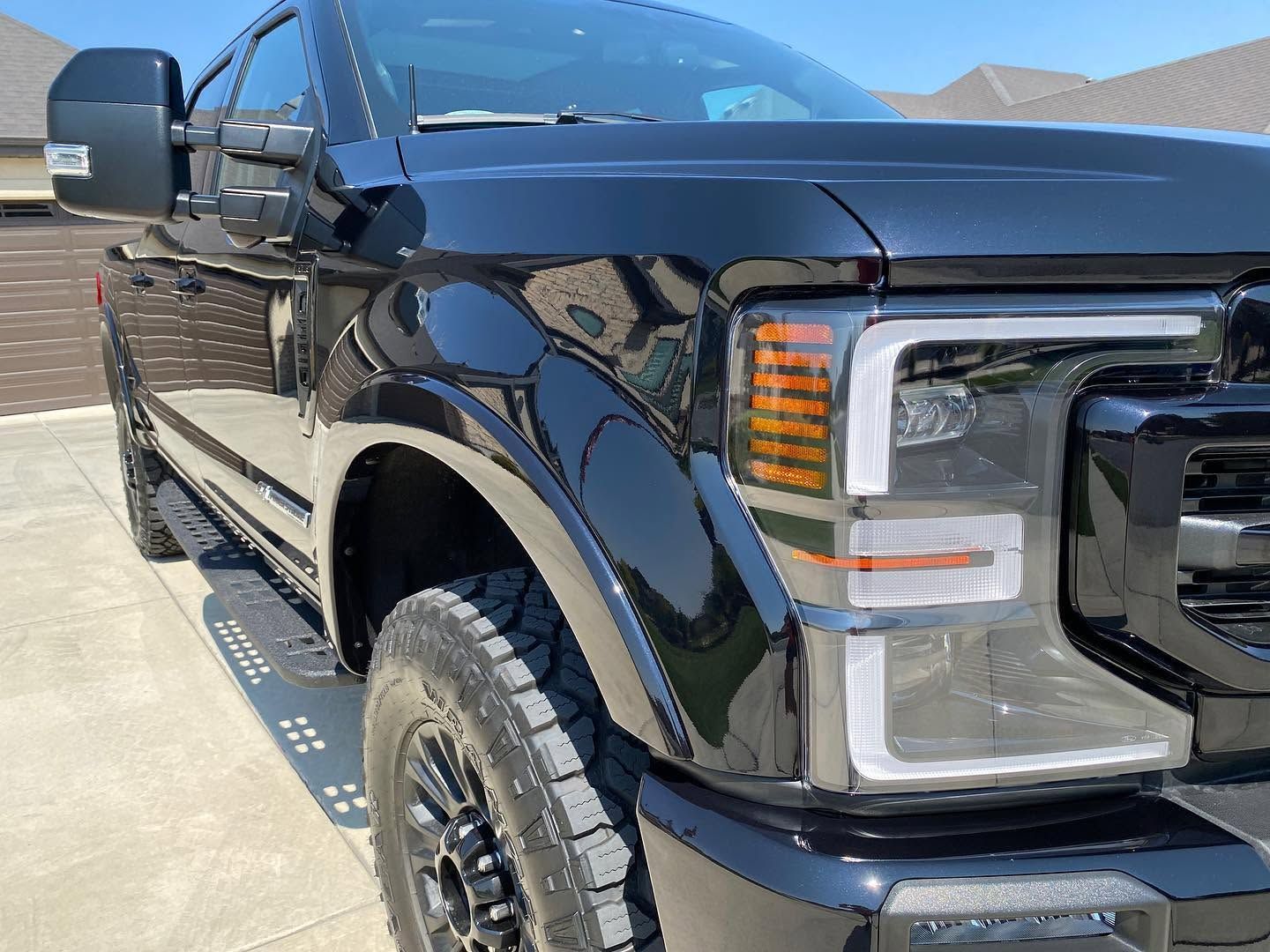 Black pickup truck parked in sunlight, front-right view with chrome grille and large side mirror