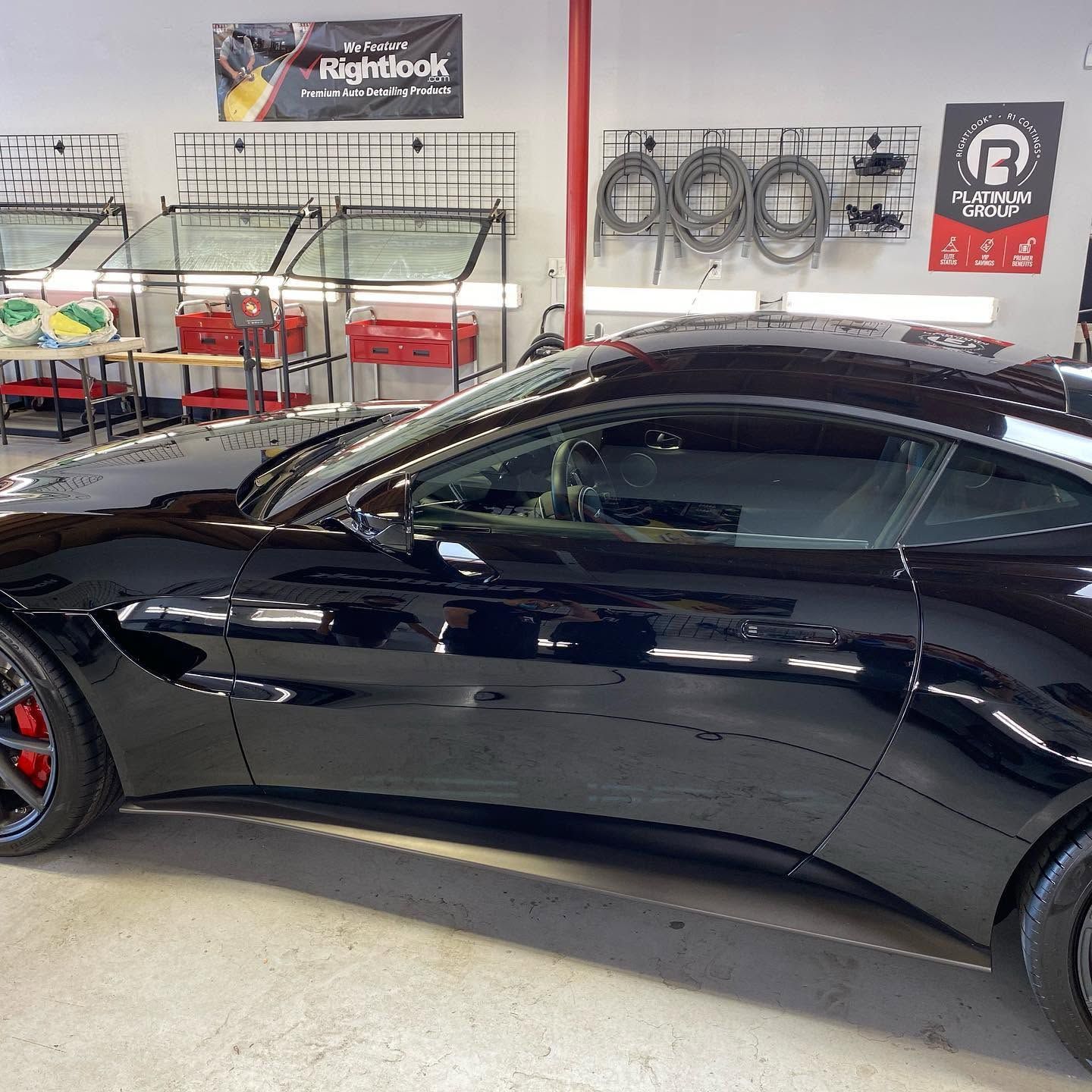 Black sports car in an auto shop, with wheels and tools displayed on the wall behind it