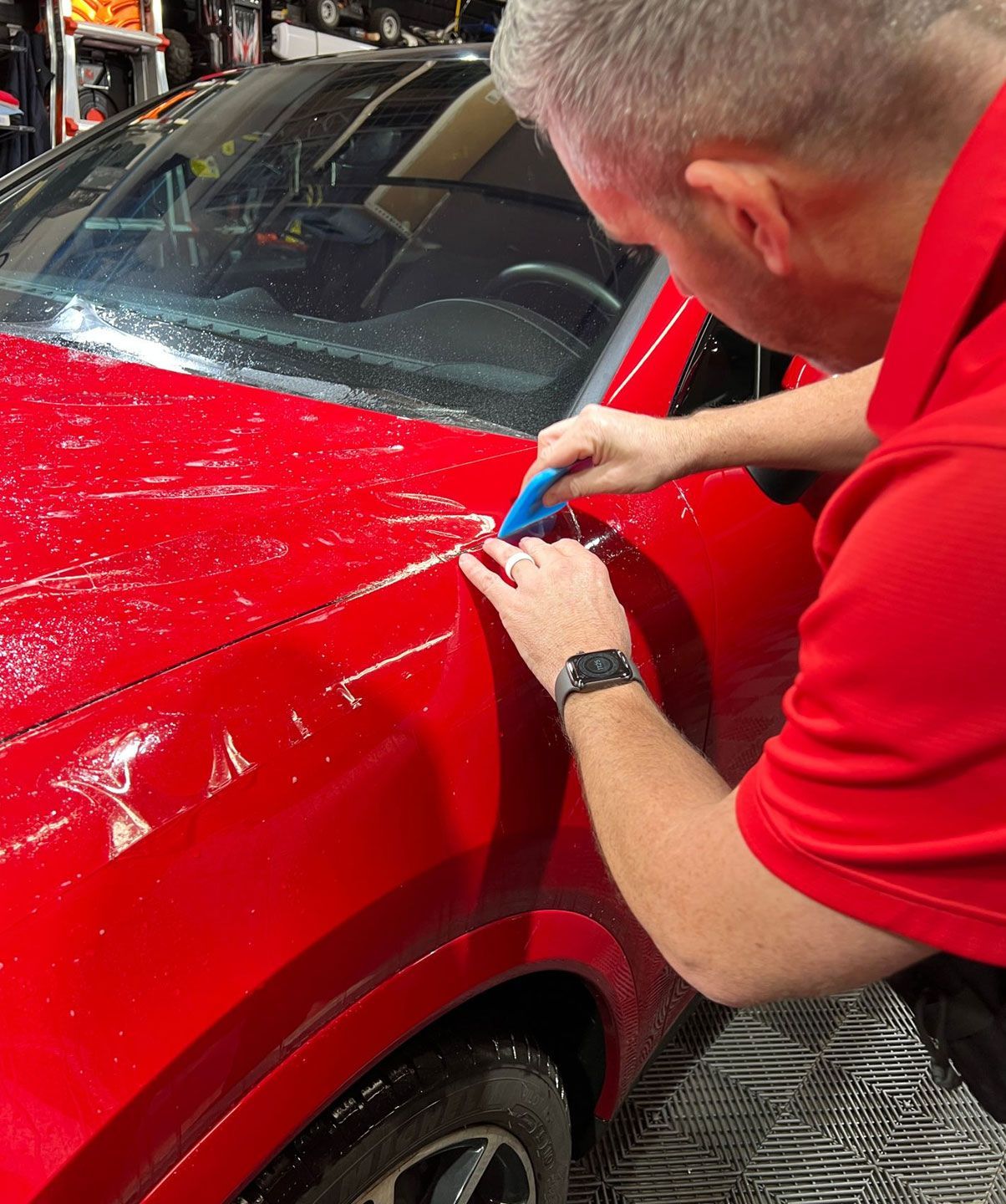 A man in a red shirt is working on a red car.