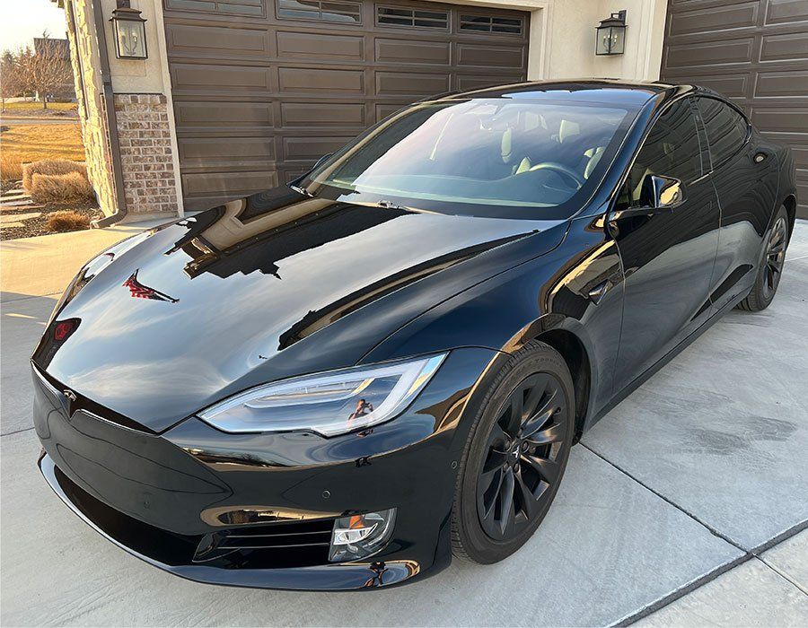 A black tesla model s is parked in front of a garage door.