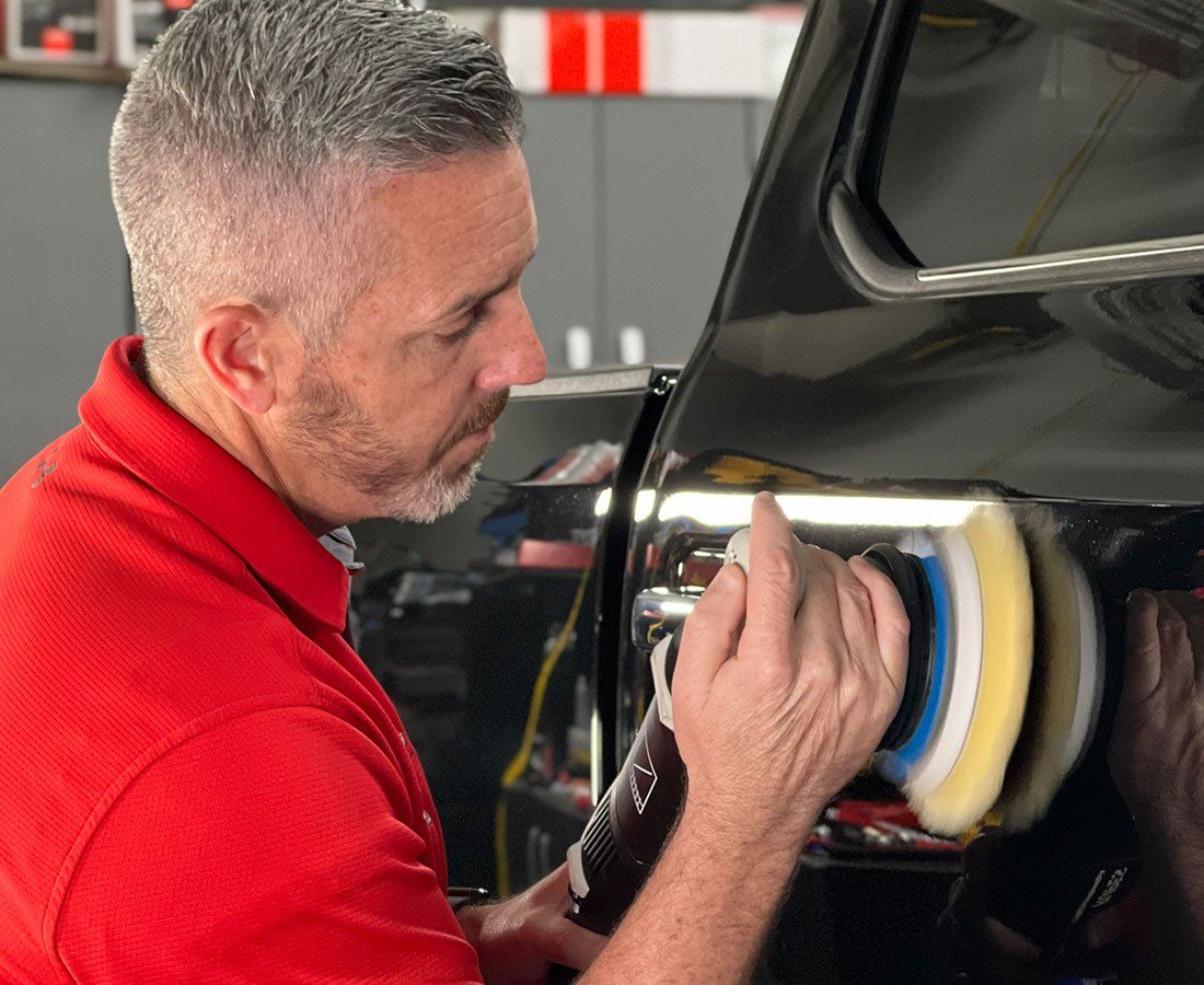 A man in a red shirt is polishing a black car