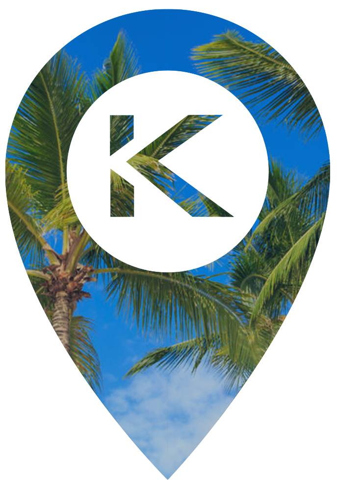 A map pin icon with a white background and the letter "K" in the center, overlaid on a blue sky with palm tree leaves.