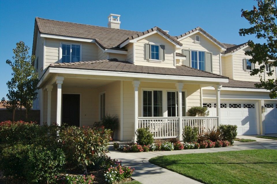 Suburban two-story beige house with a front porch, white trim, and a manicured lawn