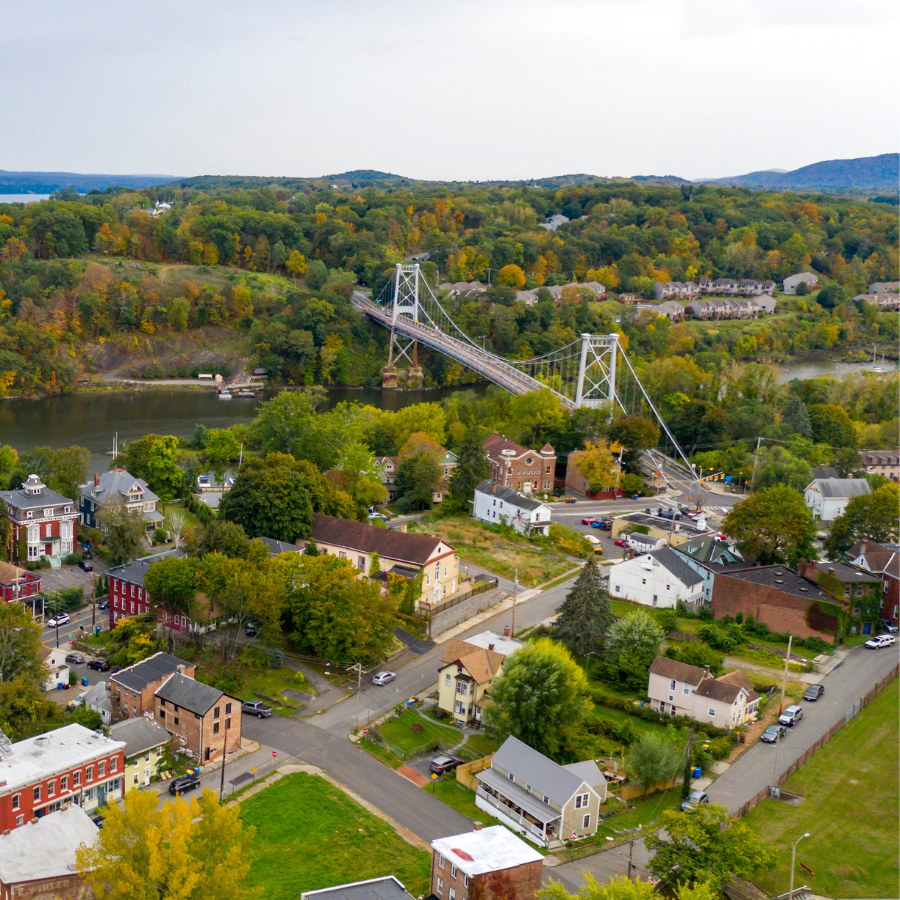 Aerial view of a town with a suspension bridge over a river, surrounded by autumn trees and hills