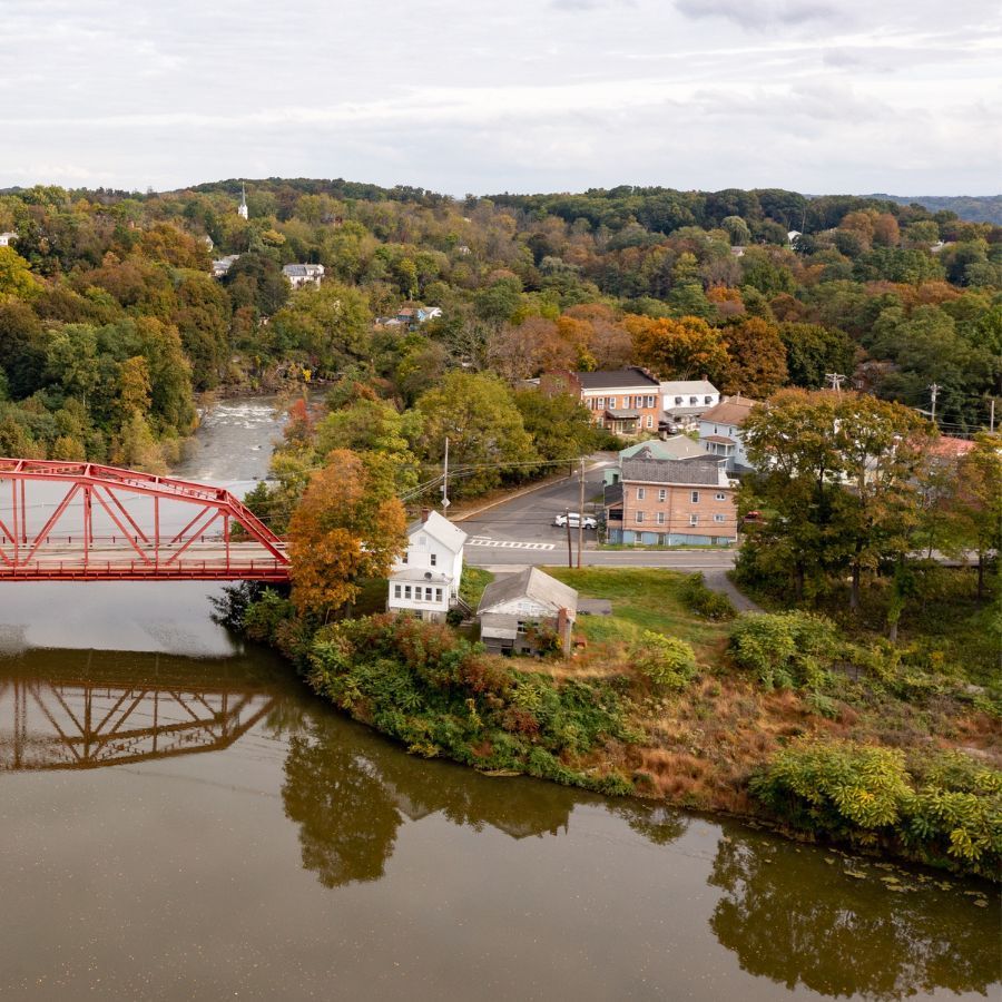 Red bridge over a river beside a small town with autumn trees on wooded hills