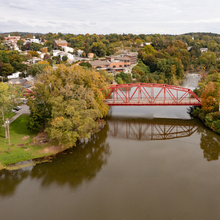 Red bridge over a calm river with trees and houses in a suburban landscape