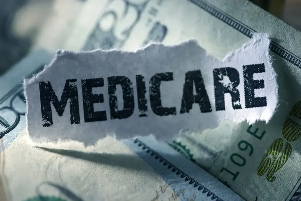 Torn paper labeled “MEDICARE” over U.S. currency bills