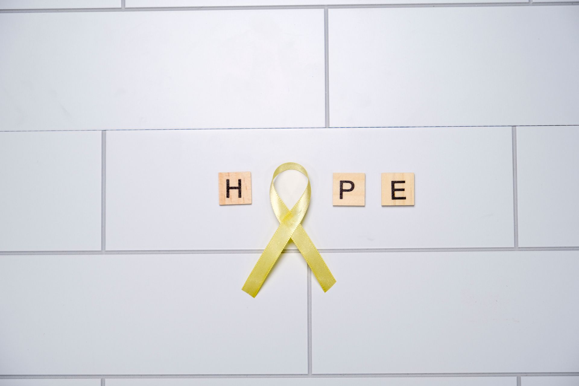 Yellow ribbon with the word “HOPE” spelled around it on a white tiled wall.
