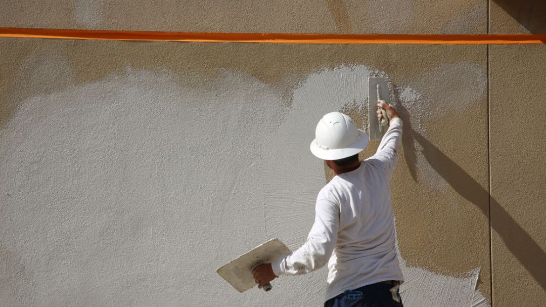 A man wearing a hard hat is plastering a wall with a trowel.