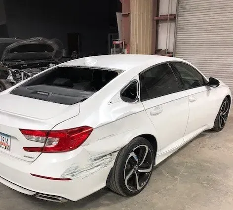 White sedan with rear-right damage and black rims parked in a garage