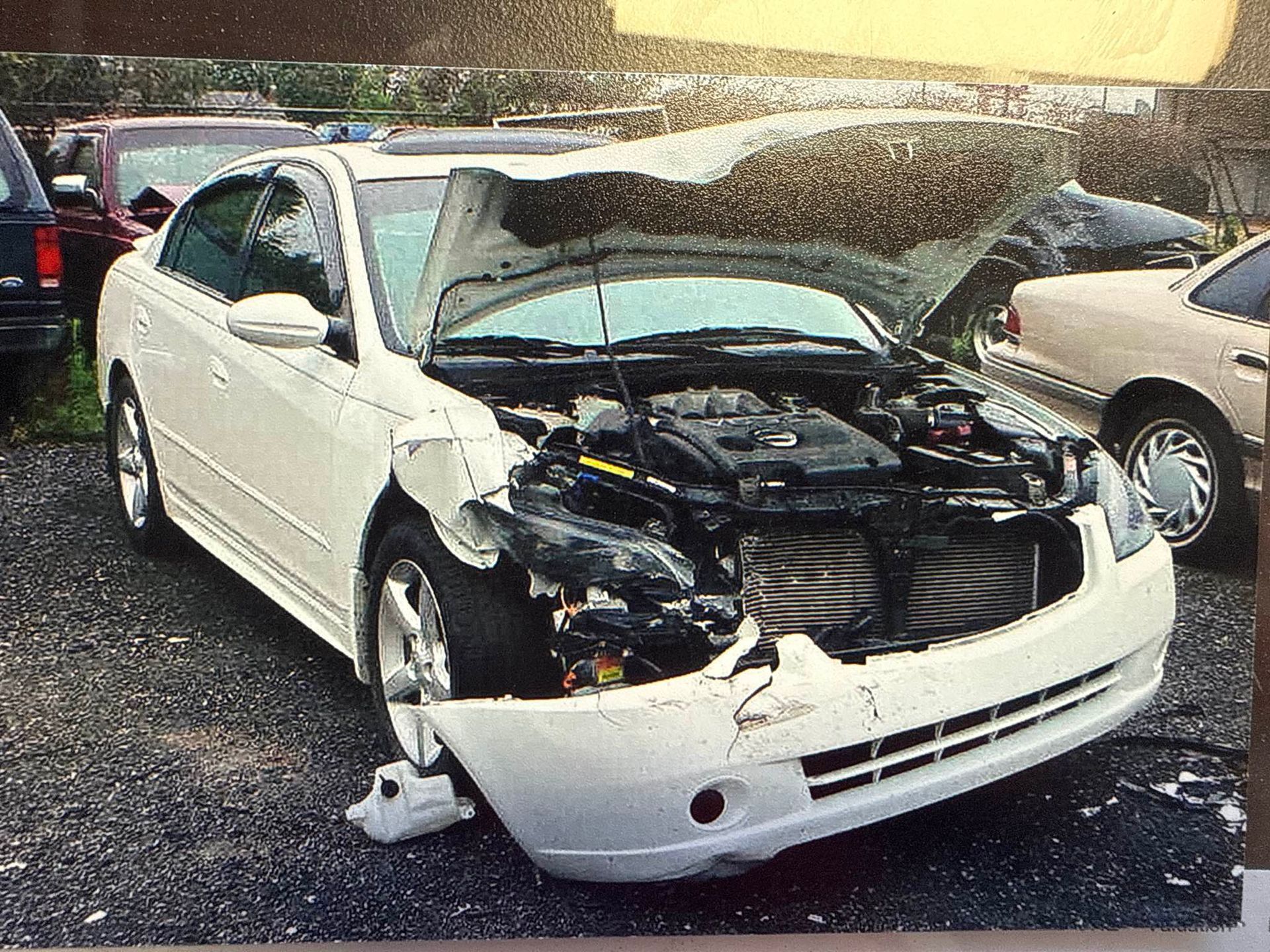 White car with front-end damage and hood open in a parking lot after a crash