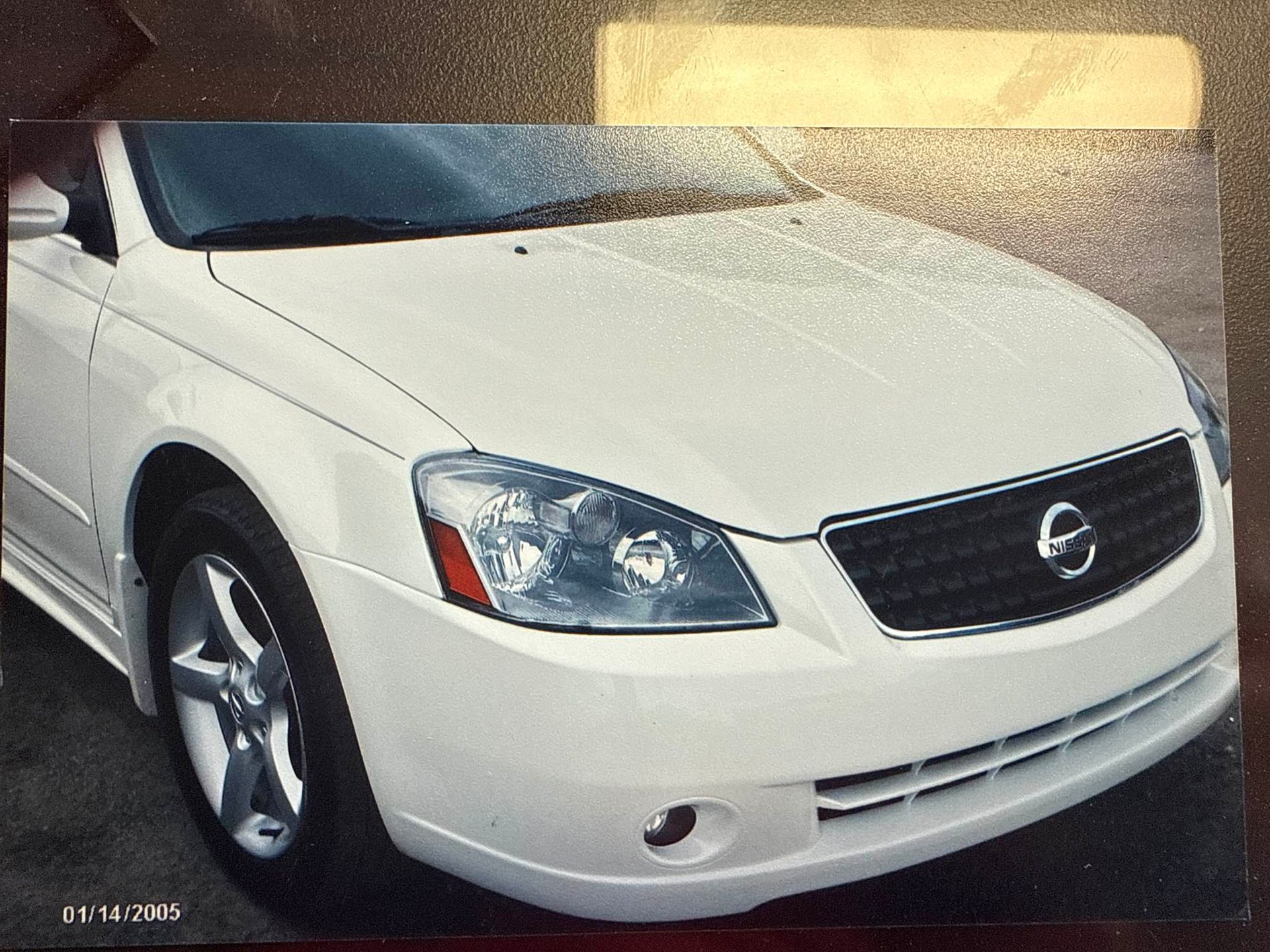 White Nissan sedan front-left view, parked indoors with chrome grille and silver wheels