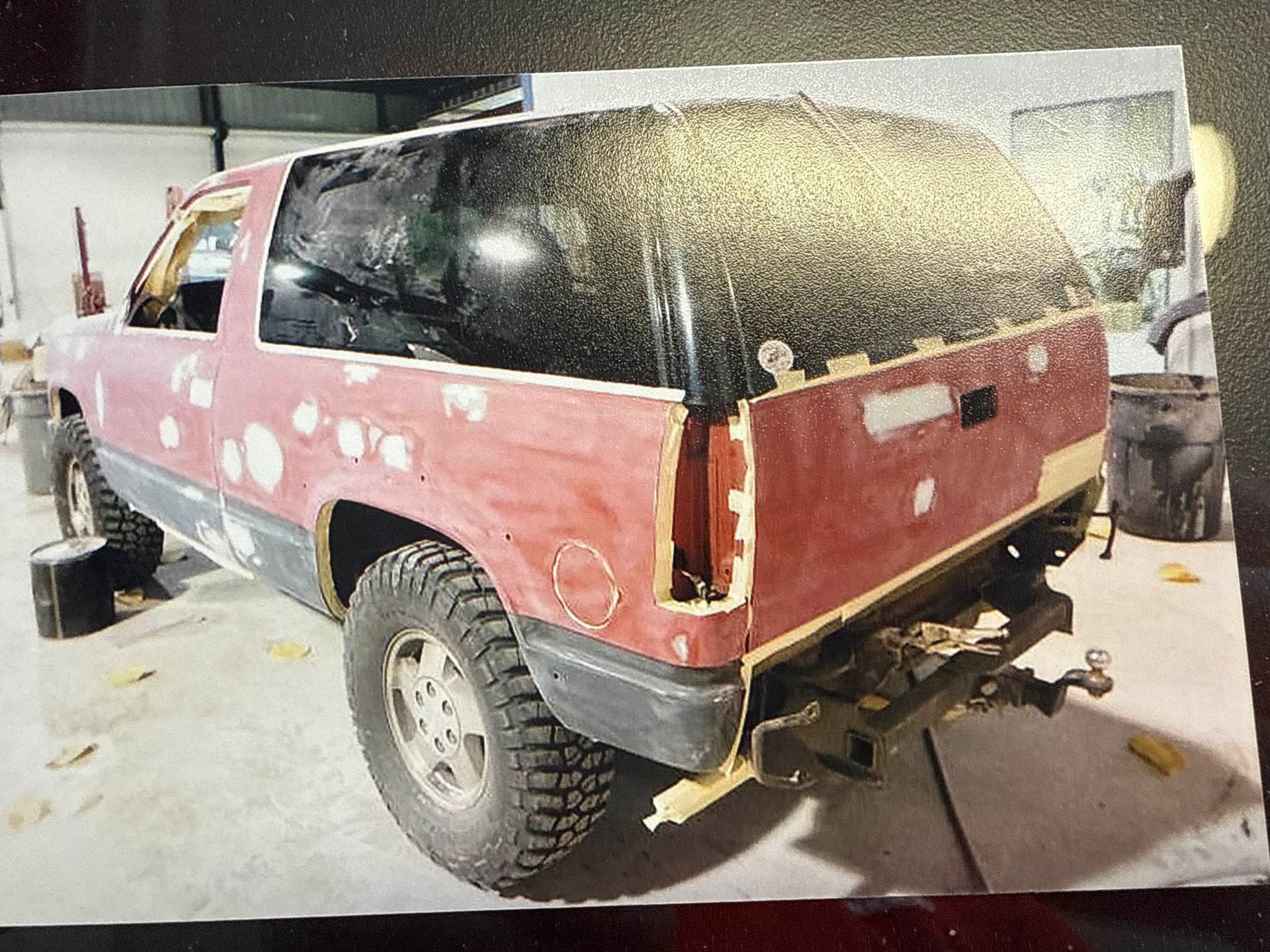 Red SUV in a workshop, rear and side panels stripped for body repair, with dusty windows and large off-road tires