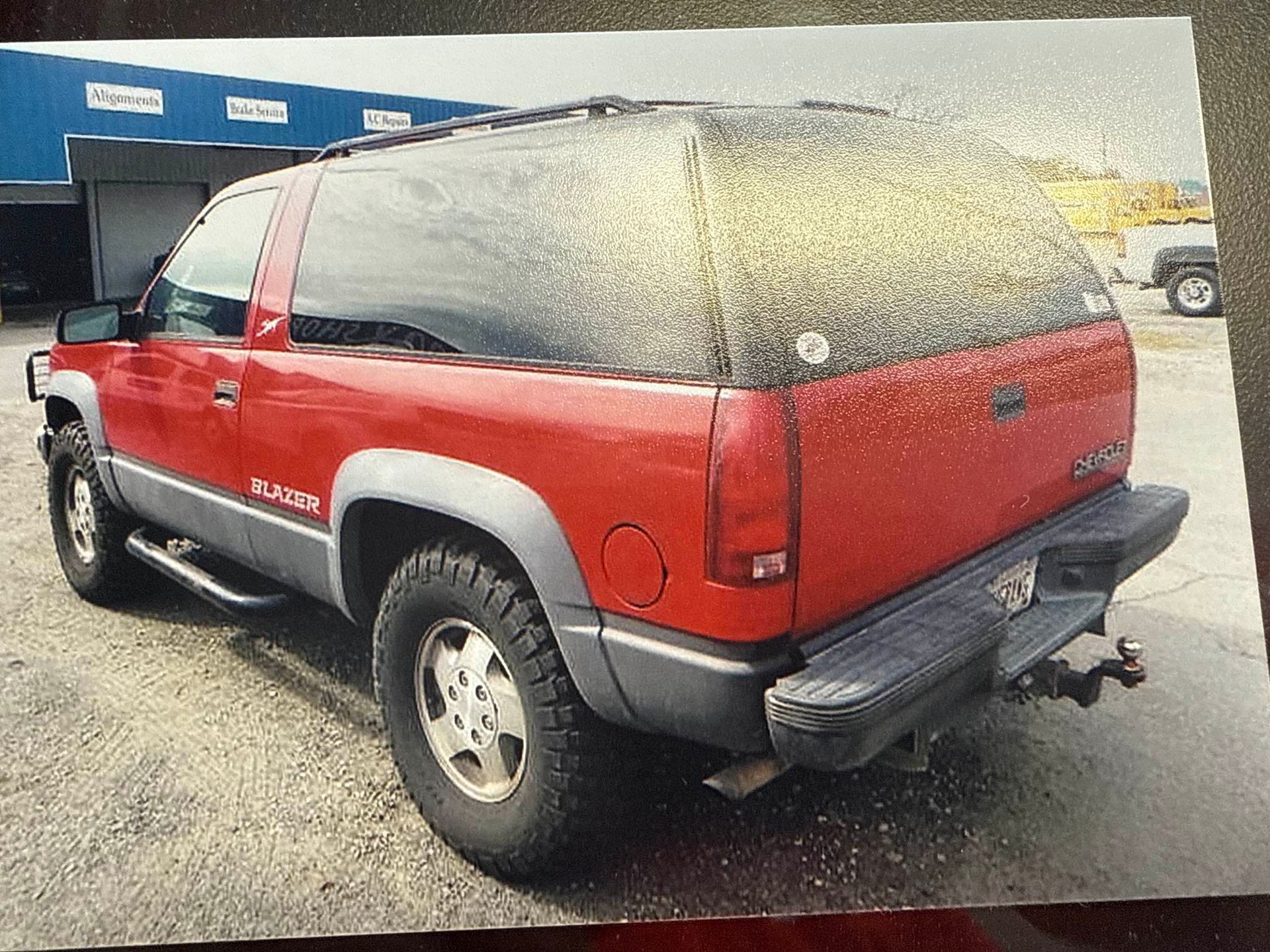 Red two-tone SUV parked on gravel outside a building, rear three-quarter view
