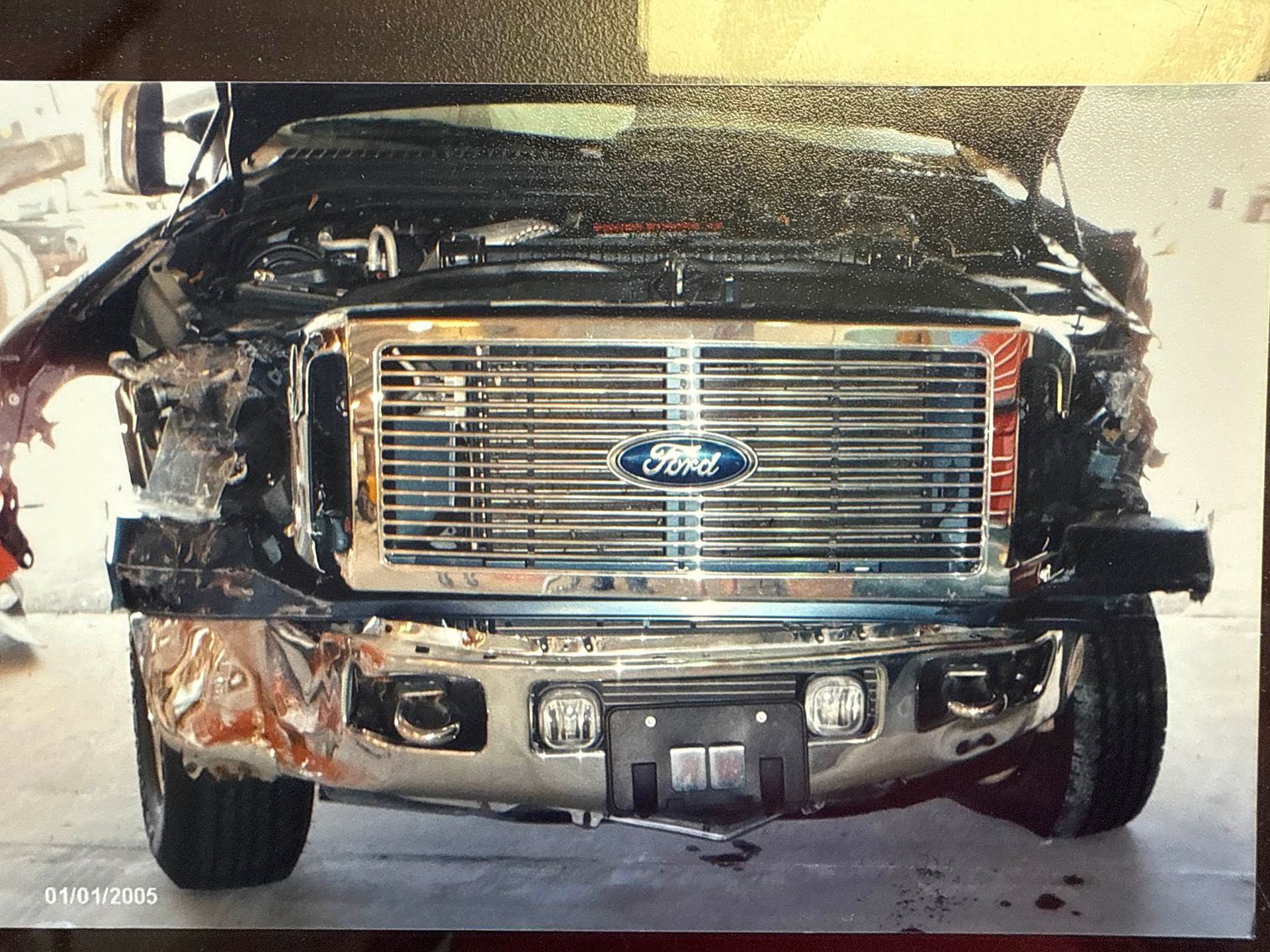 Damaged black Ford truck front with a shattered bumper and bent grille in a garage