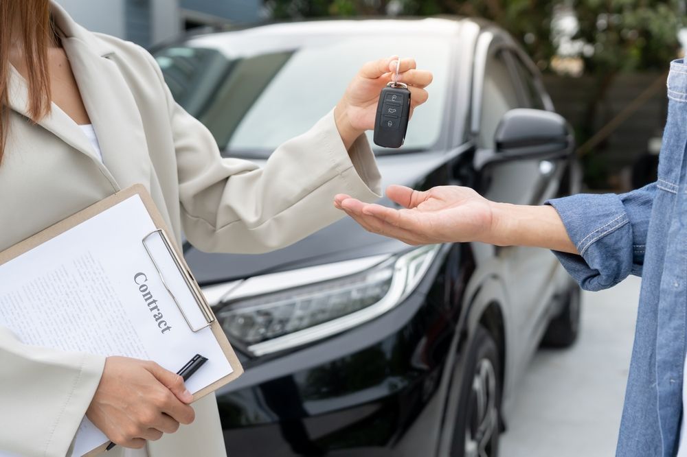 Handing car keys at a car dealership beside a black sedan
