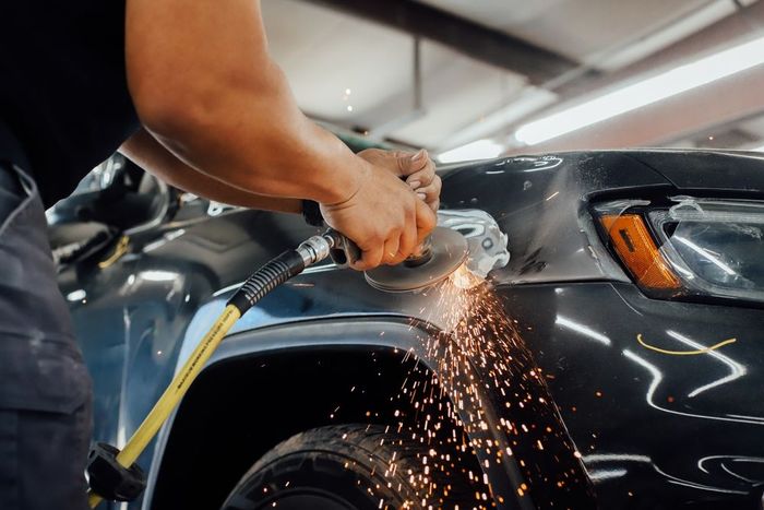 Auto body repair worker grinding a black car panel, sending sparks in a workshop