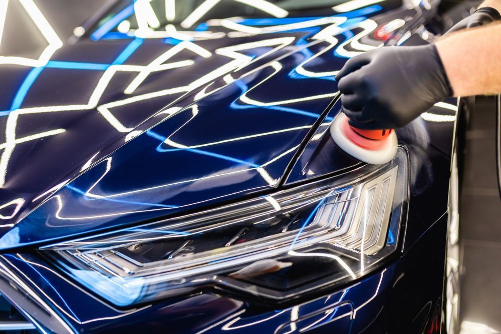 Gloved hand polishing the headlight of a dark blue car with a buffer