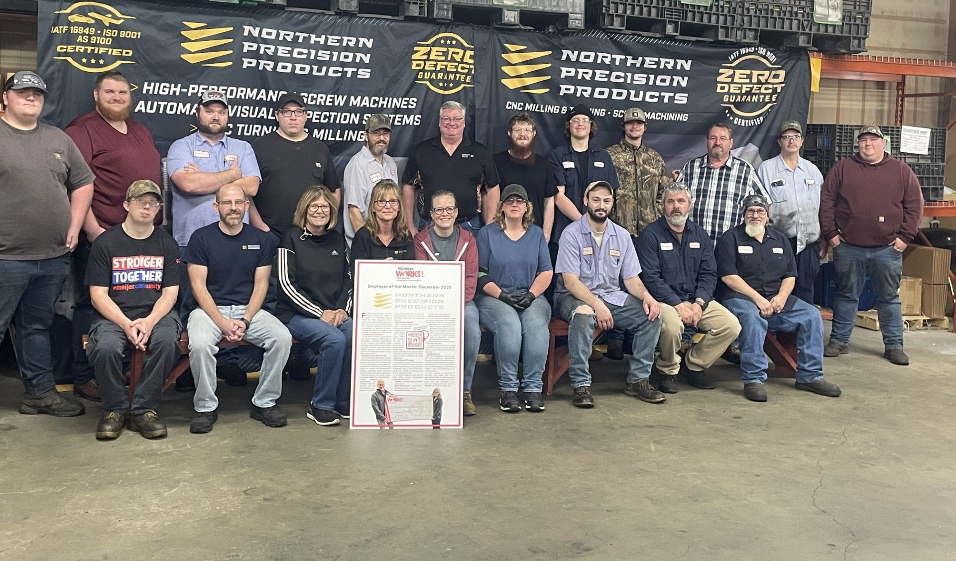 Group photo of uniformed workers and supporters in a workshop, posing with a commemorative sign.