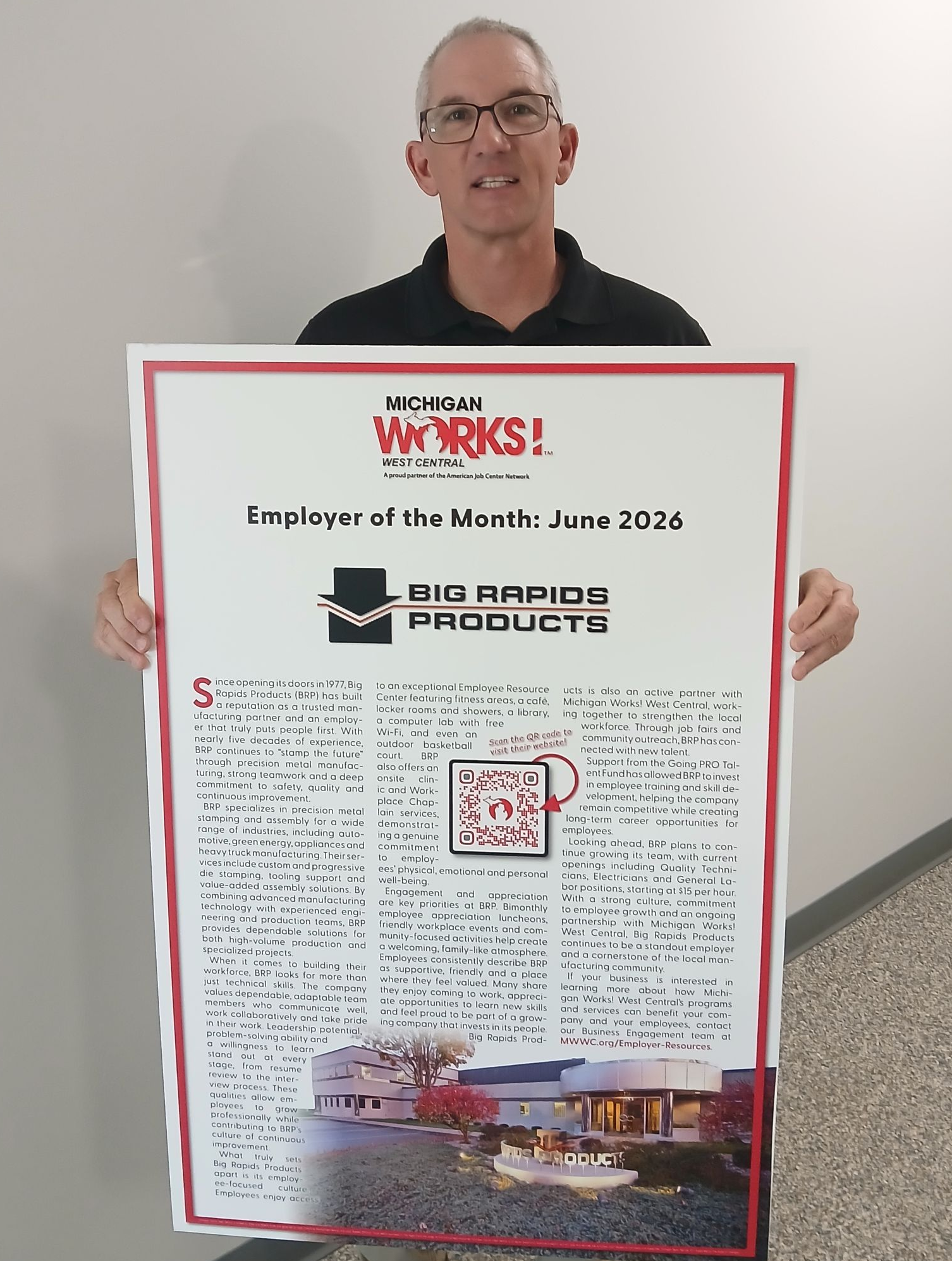 Man holding a large white poster with red border in a hallway, with dense text and a small image near the bottom.