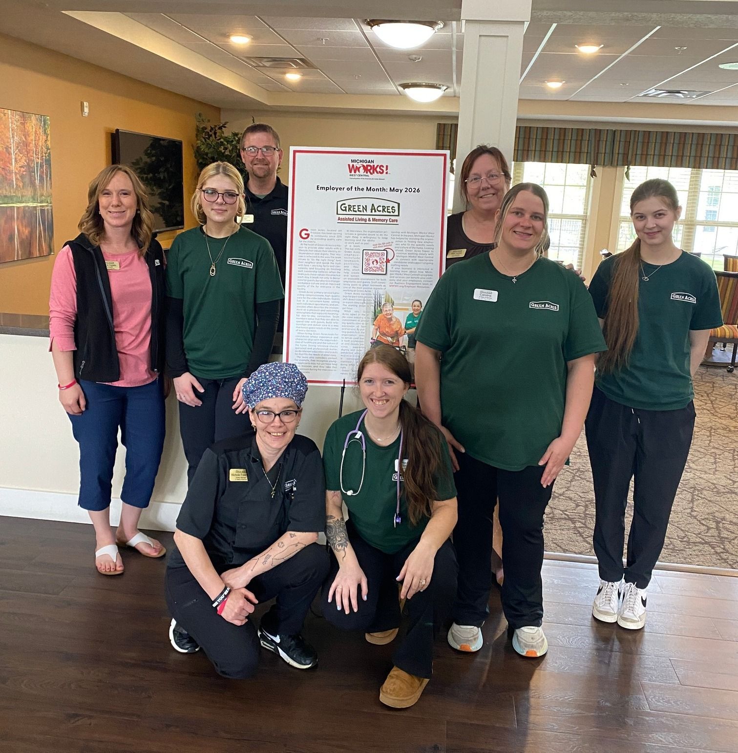 Seven people posing in a hotel lobby beside a conference poster, several wearing matching green shirts.
