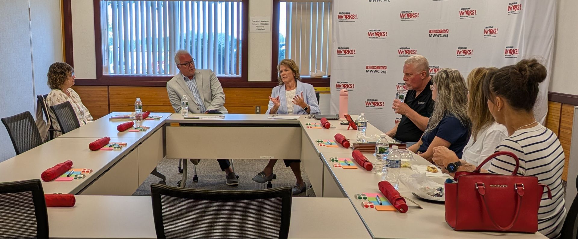 People seated around a conference table in a meeting room, with notebooks and water bottles.
