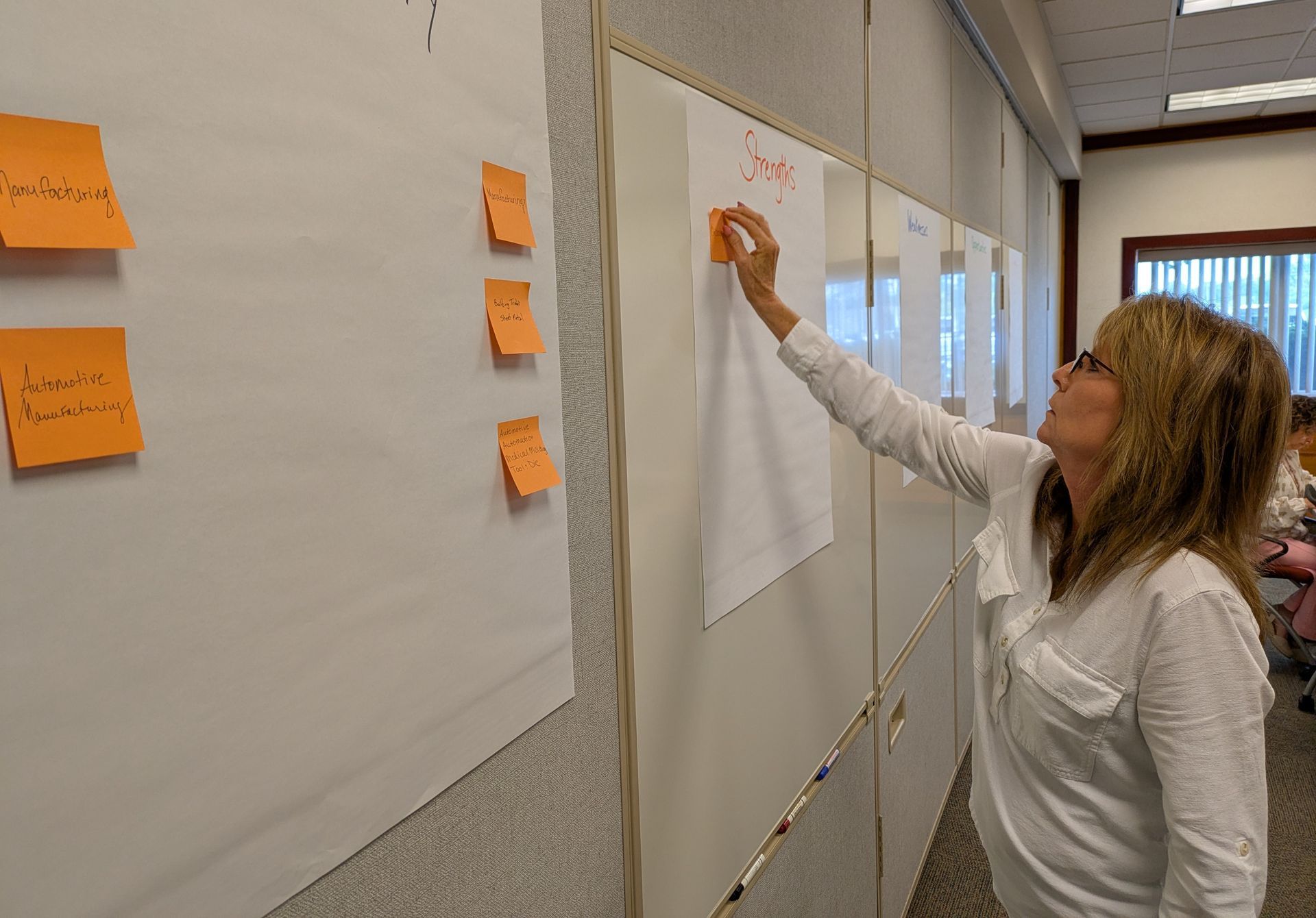 Woman placing a sticky note on a wall chart during a collaborative planning session