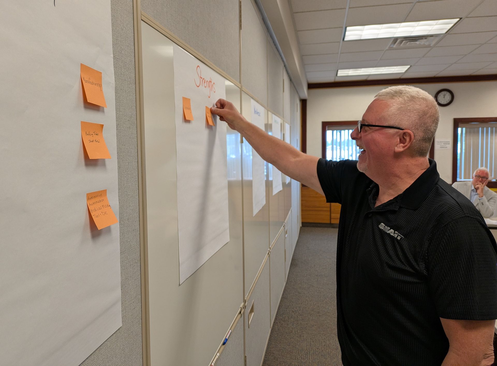 Man posting orange sticky notes on a wall chart in a meeting room