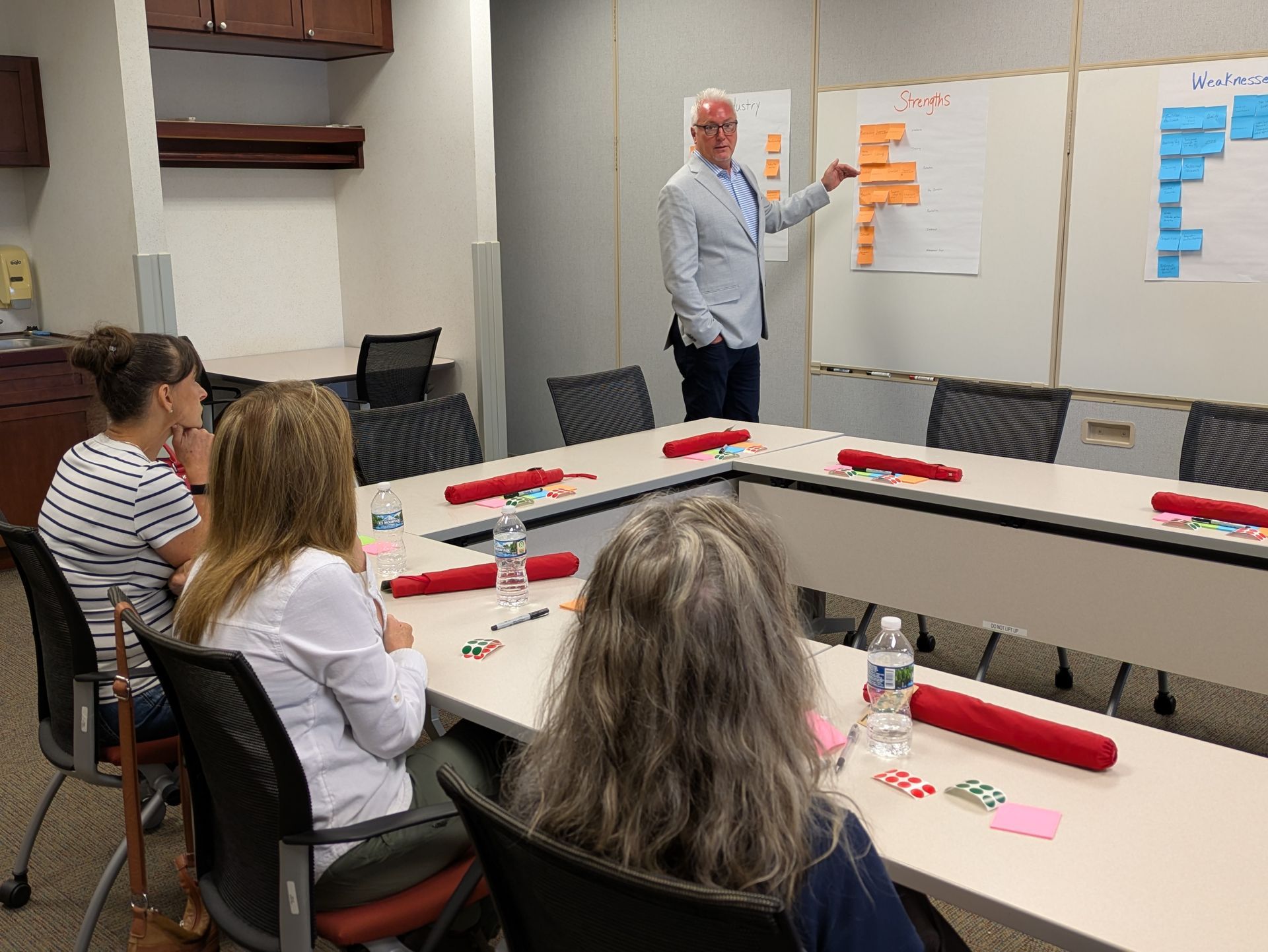 Presenter points to sticky notes during a small-group meeting in a conference room.