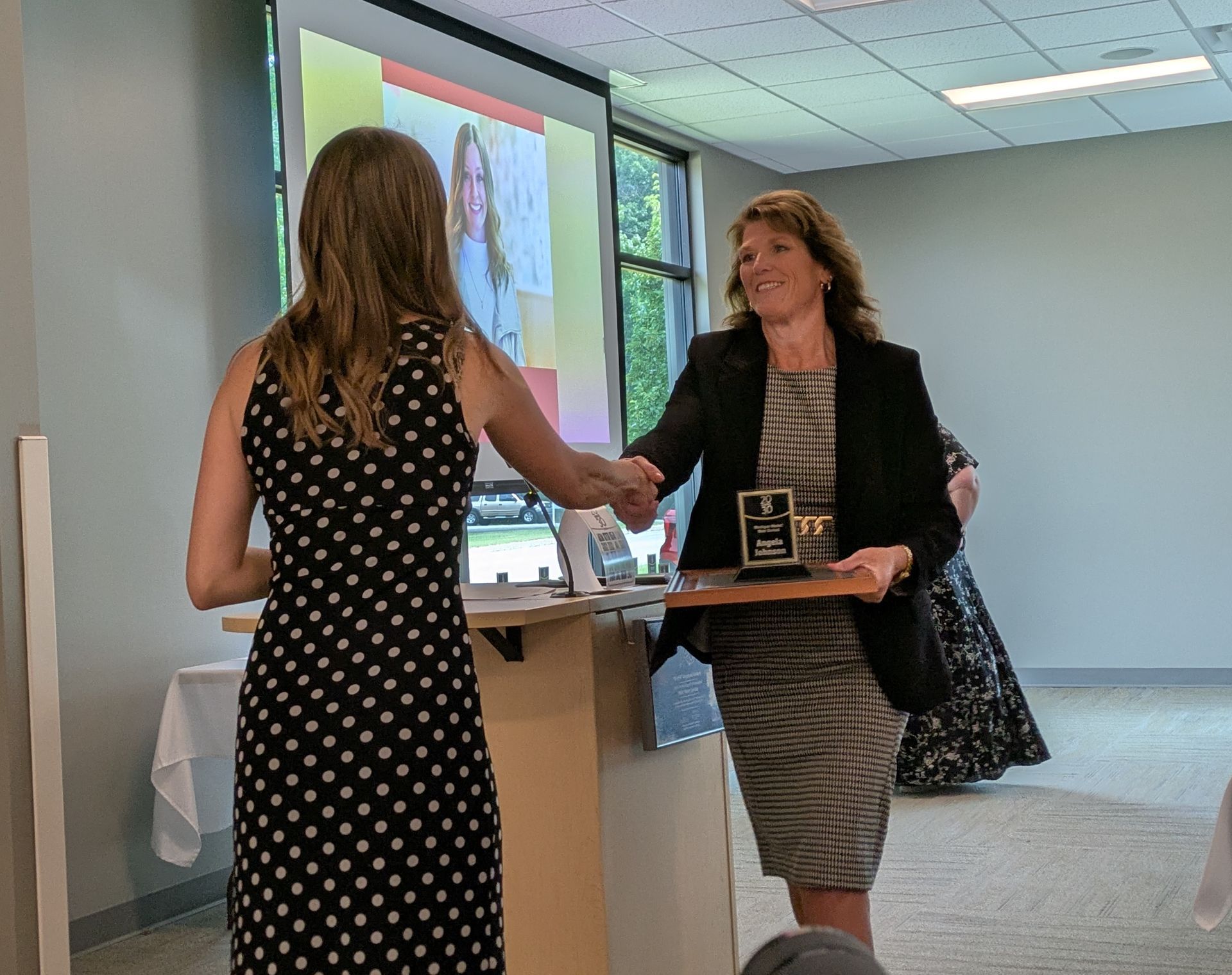 Two people shaking hands in a modern office near a presentation screen