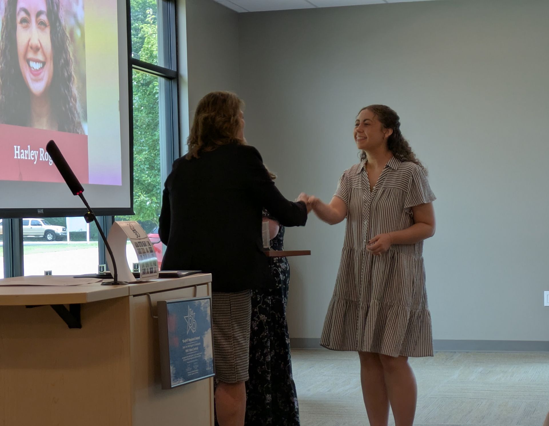 Two people exchanging an award plaque in a conference room near a projected presentation screen