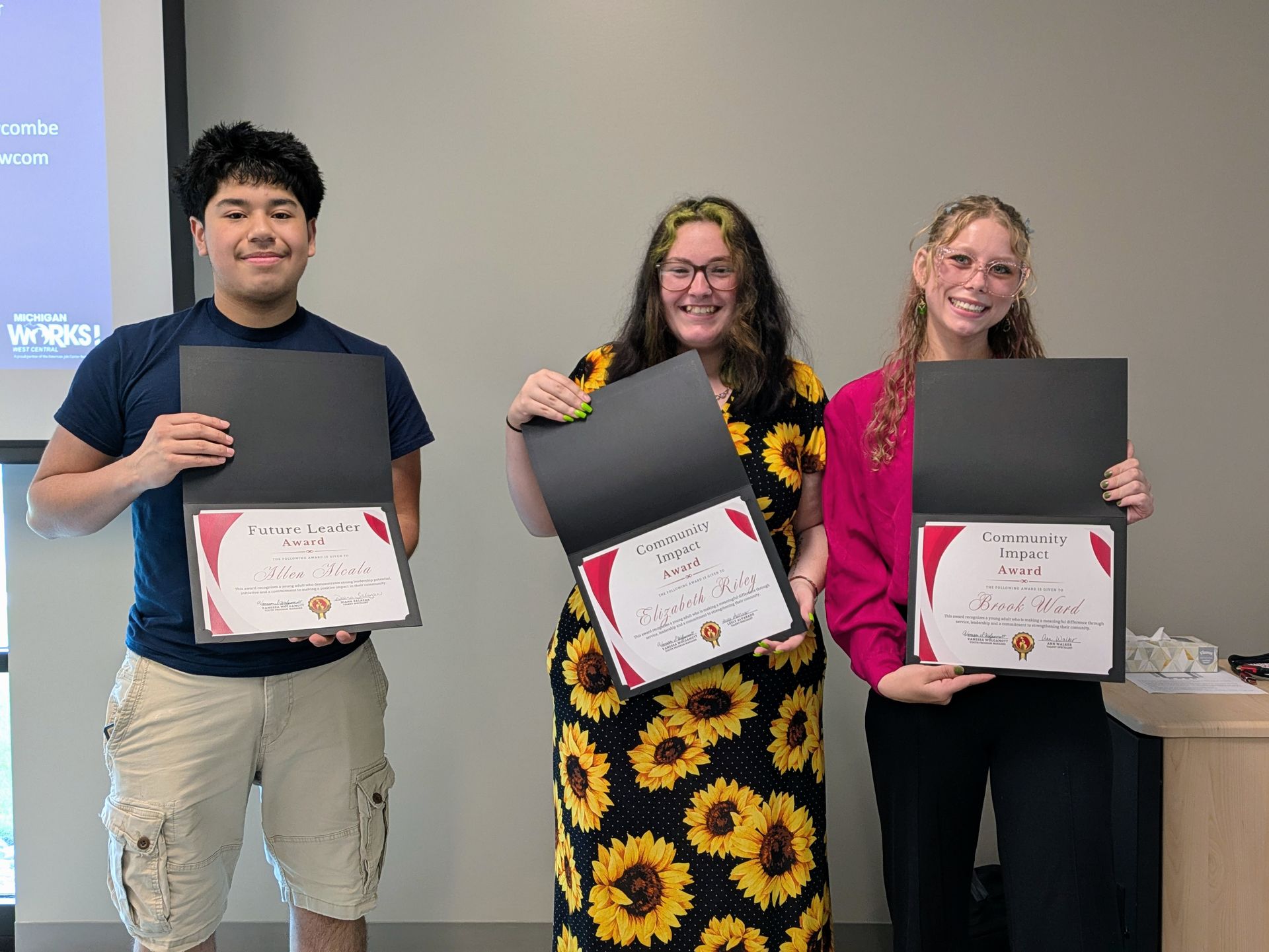 Three people smiling and holding framed certificates at an award ceremony.