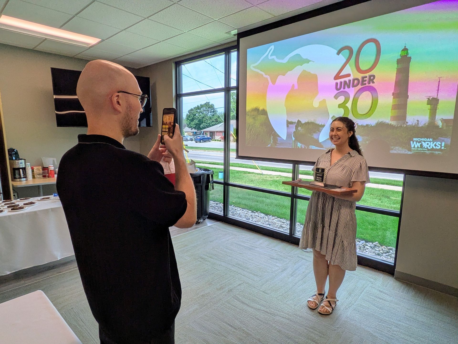 Three women posing with certificates while a person photographs them in an office hallway.